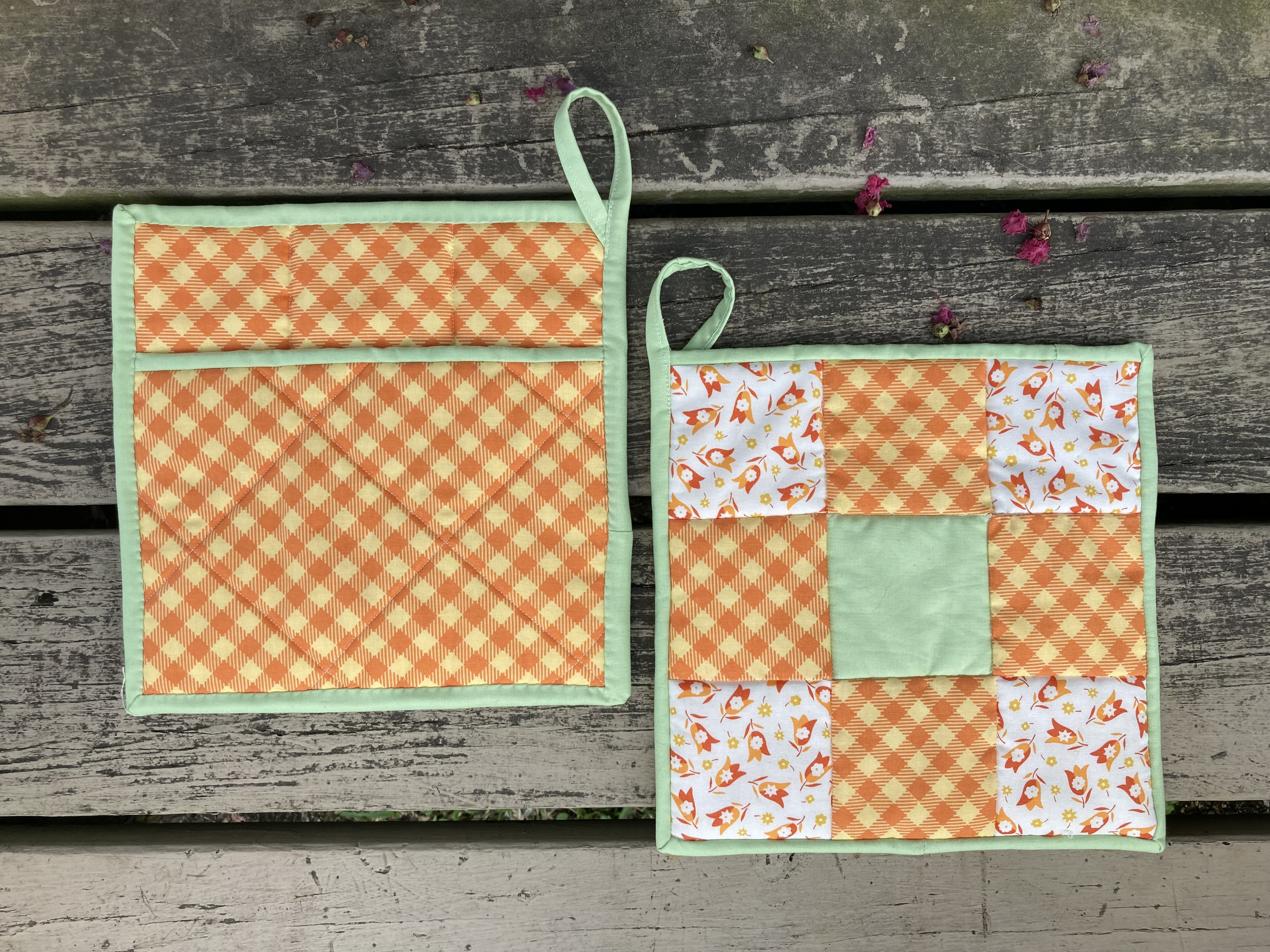 two quilted potholders with orange, white, yellow, and green patterned patches, orange and yellow gingam back pocket, and green border