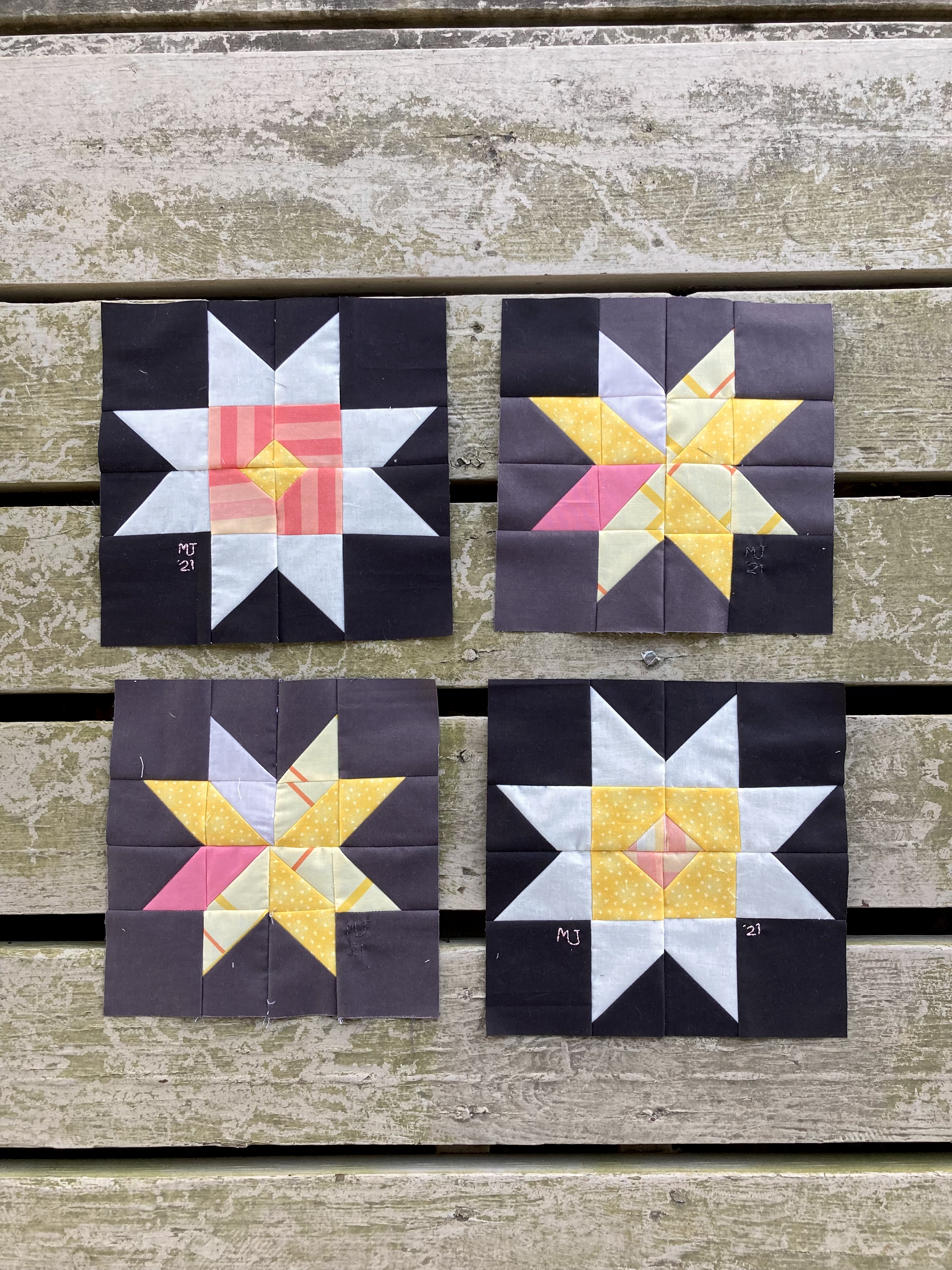 four quilt squares with star patterns in black, white, yellow, and pink